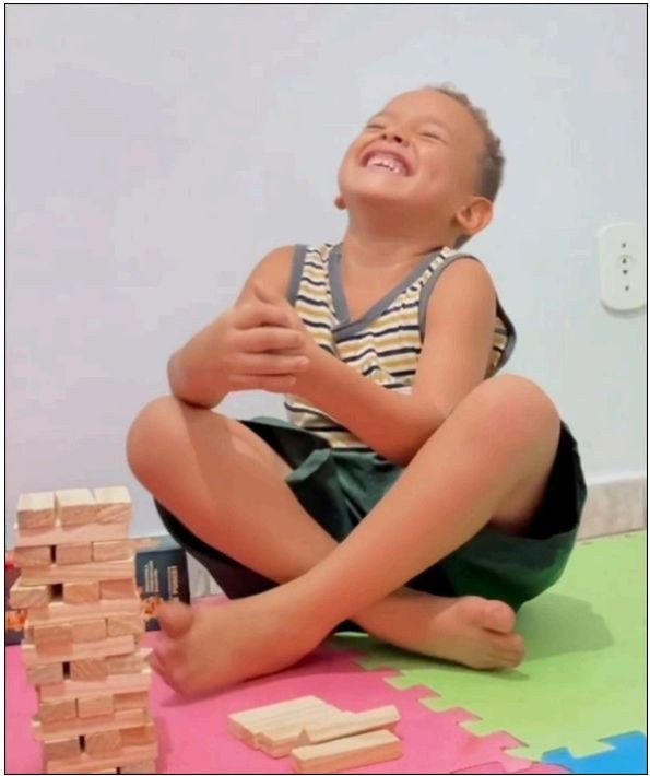 Criança sorrindo ao lado de torre de blocos de madeira