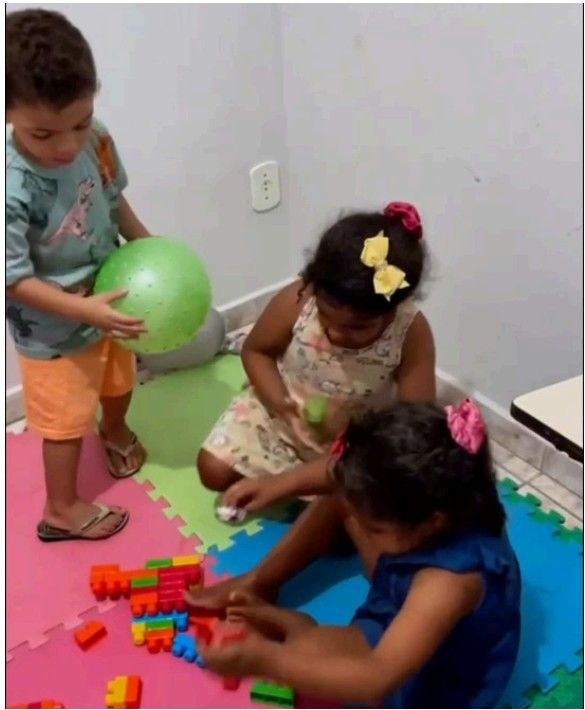 Crianças brincando com bola e blocos no tapete da sala de terapia